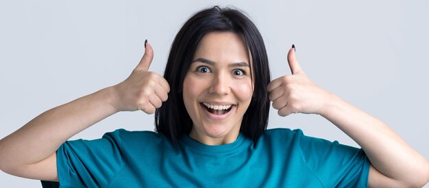 Mulher jovem e feliz, branca, com uma camiseta azul, fazendo sinal de polegar para cima e sorrindo. Bom trabalho, respeito