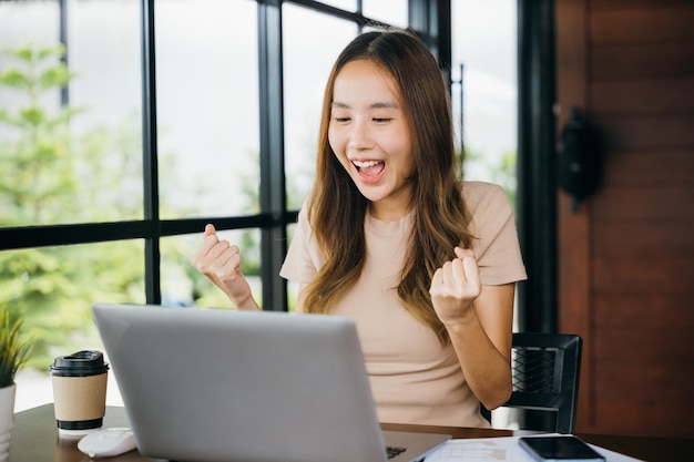 Mulher jovem e feliz em negócios asiáticos sentada com computador portátil