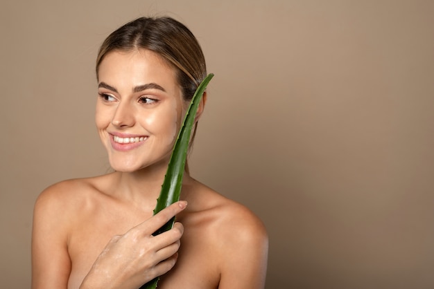 Mulher jovem e feliz sorridente segurando folha de aloe vera nas mãos em bege