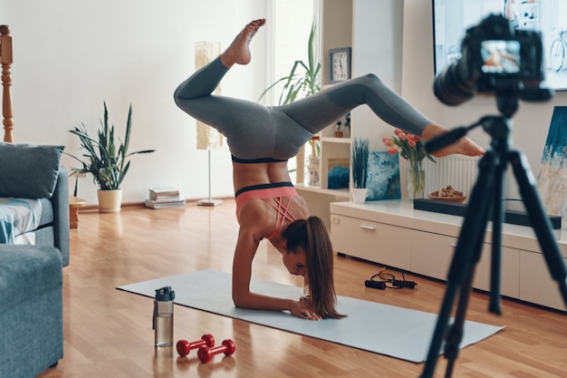 Mulher jovem e flexível em roupas esportivas, apoiada nas mãos enquanto faz um vídeo nas redes sociais