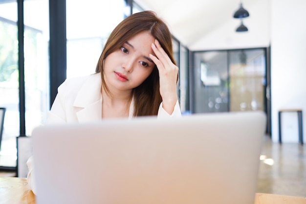 Mulher jovem e frustrada cansada trabalhando no laptop por muito tempo, trabalhando demais no escritório, sentindo dor de cabeça.