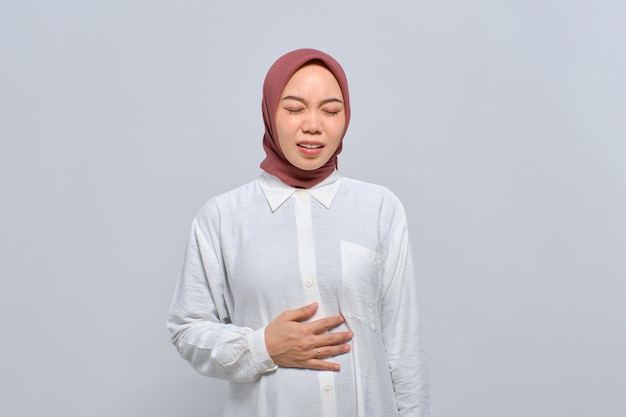 Mulher jovem e insalubre muçulmana asiática tocando barriga com dor de estômago isolada sobre fundo branco