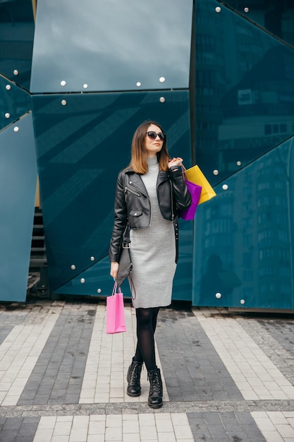 Mulher jovem e magra com sacola de compras andando perto da vitrine do shopping