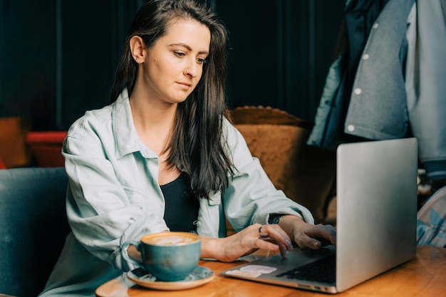Mulher jovem e moderna trabalha num café com um portátil.