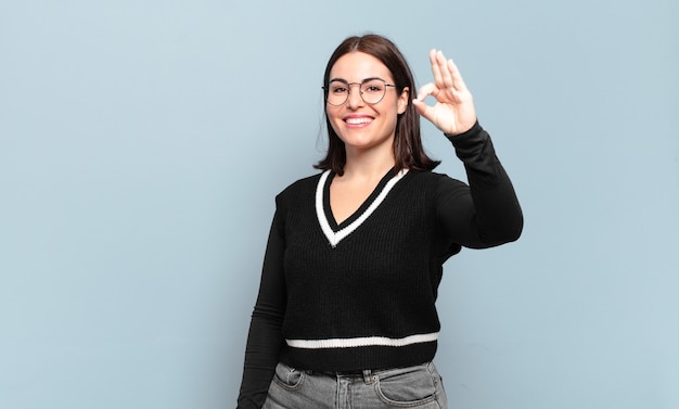 Mulher jovem e muito casual se sentindo feliz, relaxada e satisfeita, mostrando aprovação com um gesto de ok, sorrindo