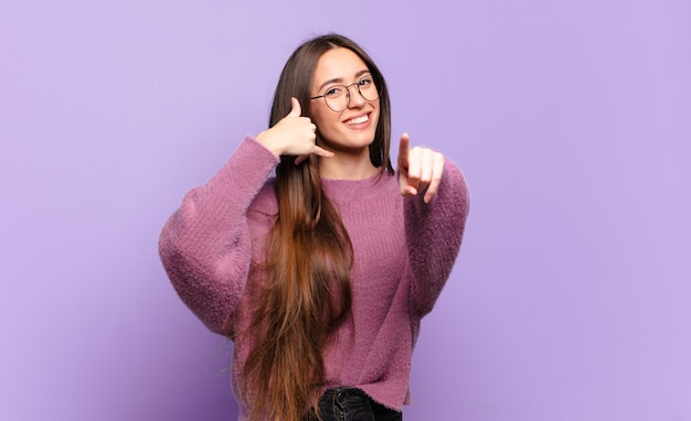 Mulher jovem e muito casual sorrindo alegremente e apontando para a frente enquanto faz um gesto de 