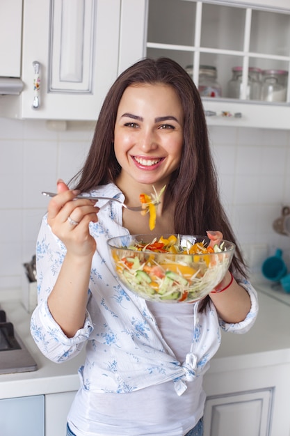 Mulher jovem e saudável comer salada na cozinha