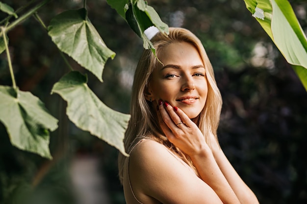 Mulher jovem e sensual caucasiana encantadora posando na floresta, aproveitando o sol e a natureza do verão, tocando o rosto, usando cosméticos orgânicos, aplicando protetor solar. cuidados com a pele, conceito de spa.