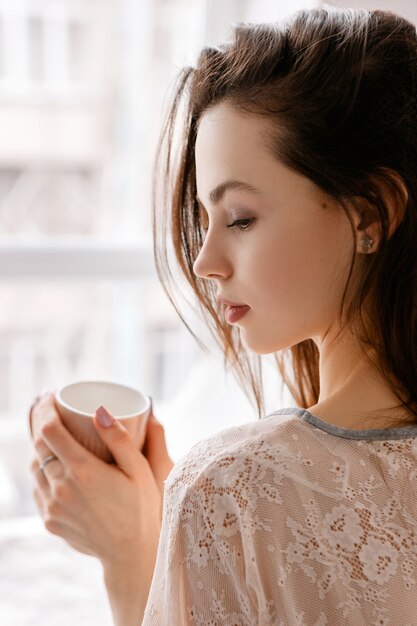 Mulher jovem e sensual com uma xícara de café na frente da janela.