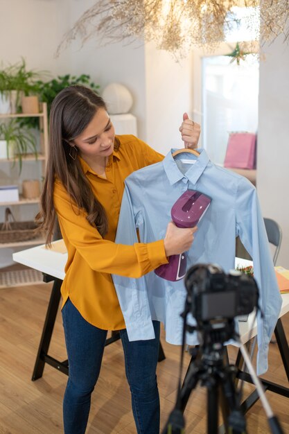 Mulher jovem e simpática em frente à câmera enquanto mostra como passar a camisa