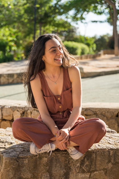 Mulher jovem e sorridente feliz sentada de pernas cruzadas Ela está sentada em um banco de pedra em um parque