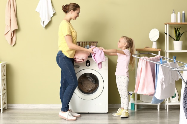 Mulher jovem e sua filha lavando roupa em casa