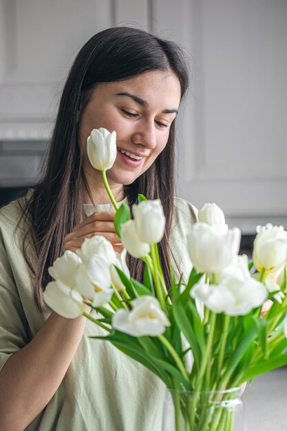 Mulher jovem e vaso com buquê de tulipas brancas na cozinha