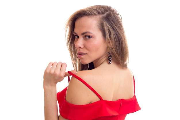 Mulher jovem elegante com cabelos castanhos compridos em vestido vermelho acanhado com brincos pretos no estúdio