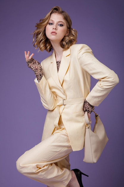 Mulher jovem elegante em calças de paletó de linho creme bege blazer handbad em fundo roxo