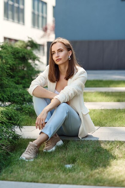 Foto mulher jovem elegante em uma roupa casual leve de pé perto da parede cinzenta do edifício moderno