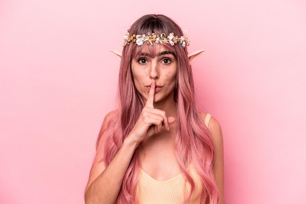 Mulher jovem elfo com cabelo rosa isolado no fundo rosa, mantendo um segredo ou pedindo silêncio.