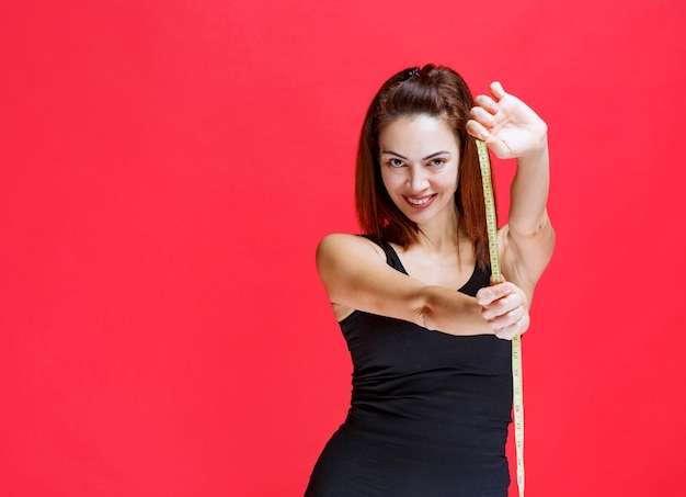 Mulher jovem em camiseta preta segurando uma fita métrica