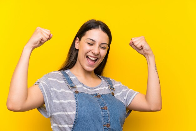 Mulher jovem, em, dungarees, isolado, ligado, amarela, celebrando, um, vitória