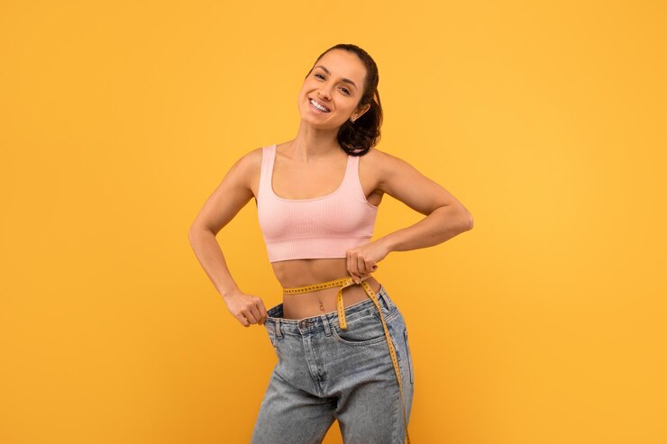 Foto mulher jovem em forma comemorando a perda de peso segurando calças jeans grandes