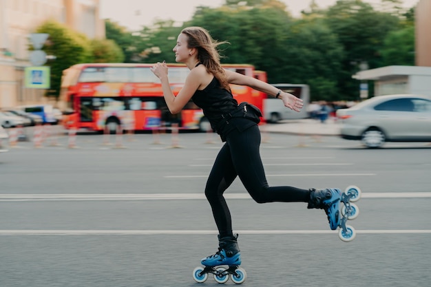 Mulher jovem em forma de patins com rodas patins durante o dia de verão na estrada movimentada com transporte leva estilo de vida ativo veste roupas esportivas pretas respira ar fresco conceito de movimento