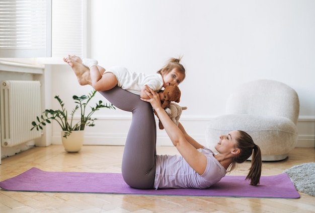 Mulher jovem em forma mãe com bebê em suas pernas fazendo fitness em tapete em casa