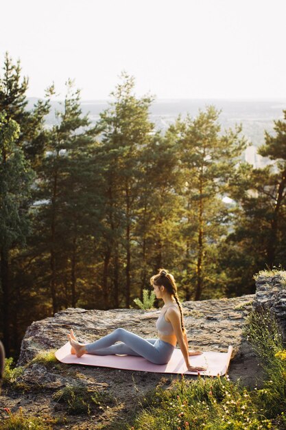 Mulher jovem em forma pratica ioga nas rochas contra o fundo da floresta de pinheiros