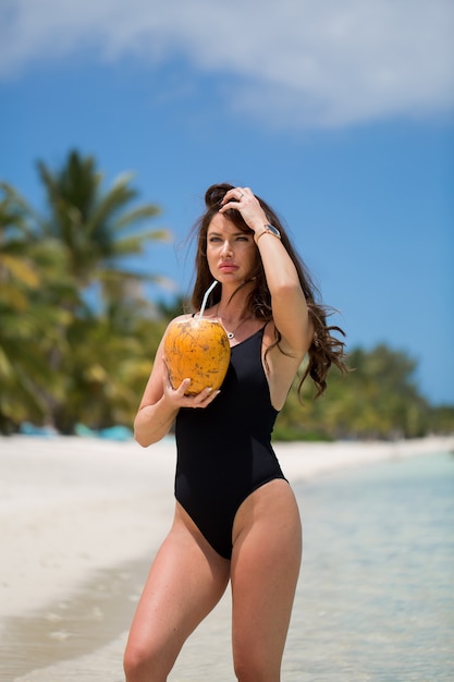 Mulher jovem em maiô preto com coquetel de coco na praia