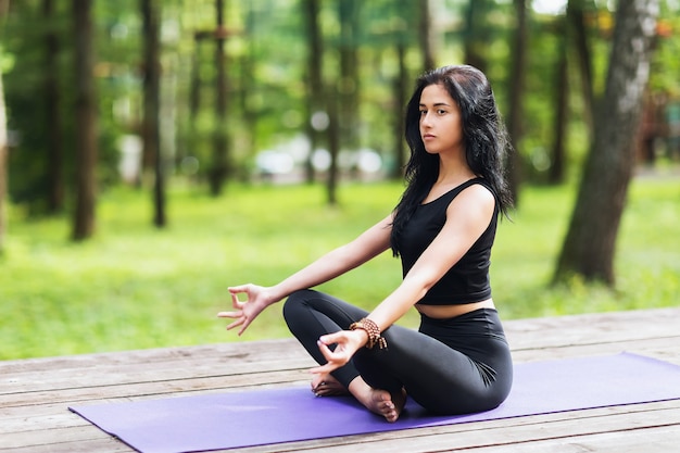 Mulher jovem em roupa esportiva preta meditando no parque em um playground de madeira