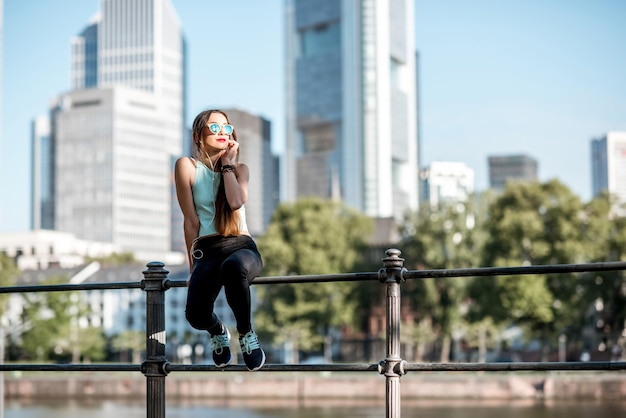 Mulher jovem em roupas esportivas, descansando em cima do muro durante o exercício matinal na cidade de Frankfurt