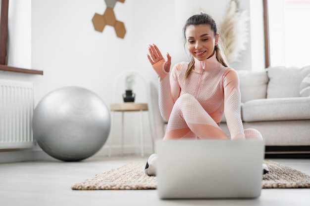 Mulher jovem em roupas esportivas usando laptop para assistir a tutoriais em vídeo de exercícios em casa