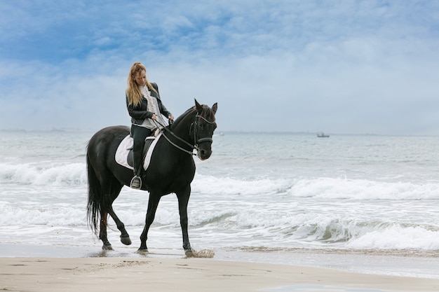 Mulher jovem em um cavalo na praia em um dia nublado