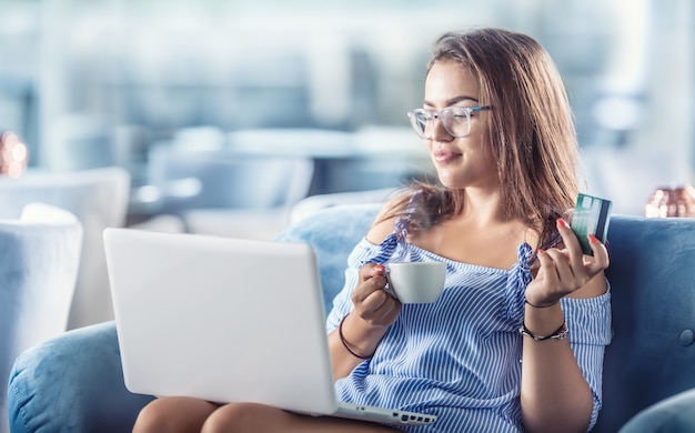 Foto mulher jovem em um cfe com um cartão de crédito e um laptop pode comprá-los confortavelmente pela internet