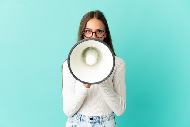 Mulher jovem em um fundo azul isolado gritando em um megafone para anunciar algo