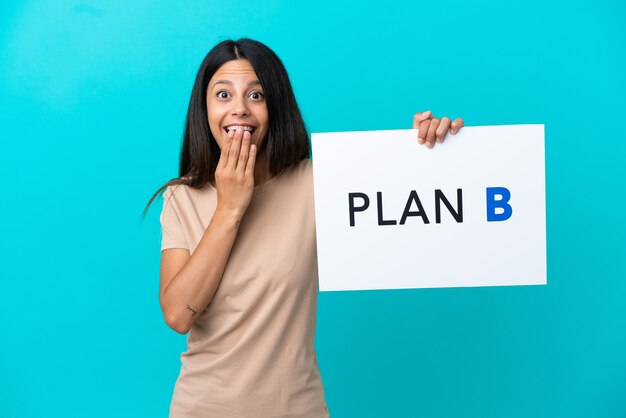 Mulher jovem em um fundo isolado segurando um cartaz com a mensagem PLANO B com expressão de surpresa