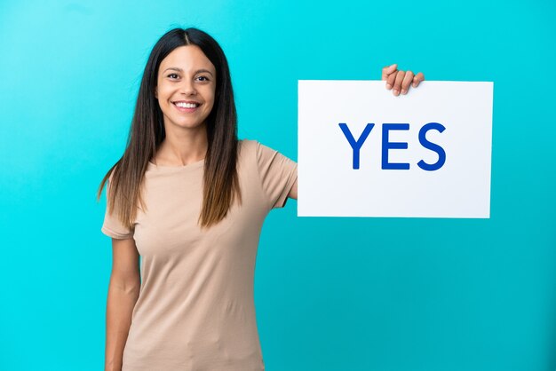 Foto mulher jovem em um fundo isolado segurando um cartaz com o texto sim com uma expressão feliz