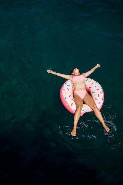 Mulher jovem em um maiô nada em um anel inflável no mar. Conceito de férias de verão.