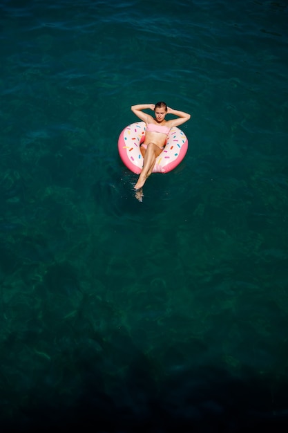 Mulher jovem em um maiô nada em um anel inflável no mar. Conceito de férias de verão.