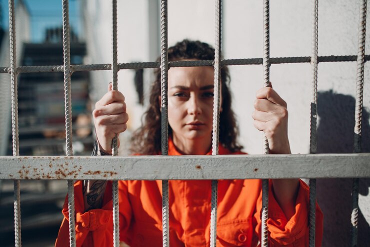 Foto mulher jovem em um terno laranja atrás das grades da prisão feminina em um macacão colorido retrato conceito de lei e justiça