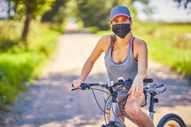 Mulher jovem em uma bicicleta no campo usando uma máscara devido à pandemia de coronavírus