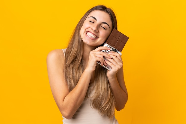 Mulher jovem em uma parede amarela isolada tomando um comprimido de chocolate e feliz