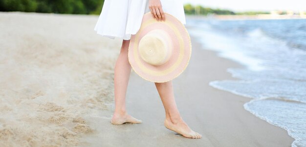 Mulher jovem em uma praia segurando um chapéu branco.