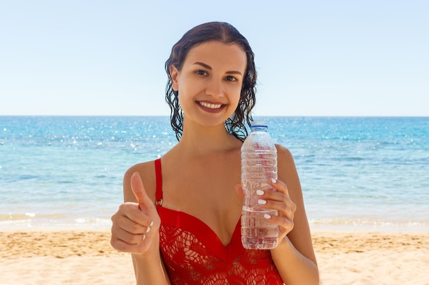 Mulher jovem, em, vermelho, fato de banho, praia, segurando, um, garrafa água