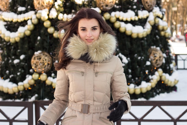 Mulher jovem em winter park perto de uma árvore de natal ao ar livre