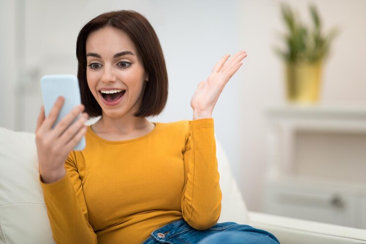 Foto mulher jovem emocional sentada no sofá em casa usando smartphone