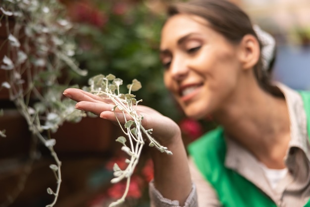 Mulher jovem empreendedora de avental verde verificando flores em uma estufa.