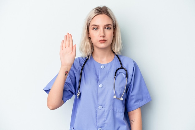 Mulher jovem enfermeira isolada em um fundo azul em pé com a mão estendida, mostrando o sinal de stop, impedindo você.