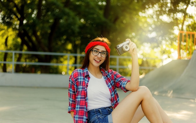 Mulher jovem engraçada com roupas elegantes e usando câmera retro no skatepark em um dia ensolarado