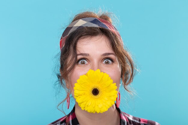 Mulher jovem engraçada e positiva em imagem retrô segurando uma flor gerbera amarela brilhante entre os dentes