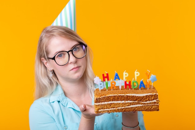 Mulher jovem engraçada e positiva tem nas mãos um bolo caseiro com a inscrição feliz aniversário